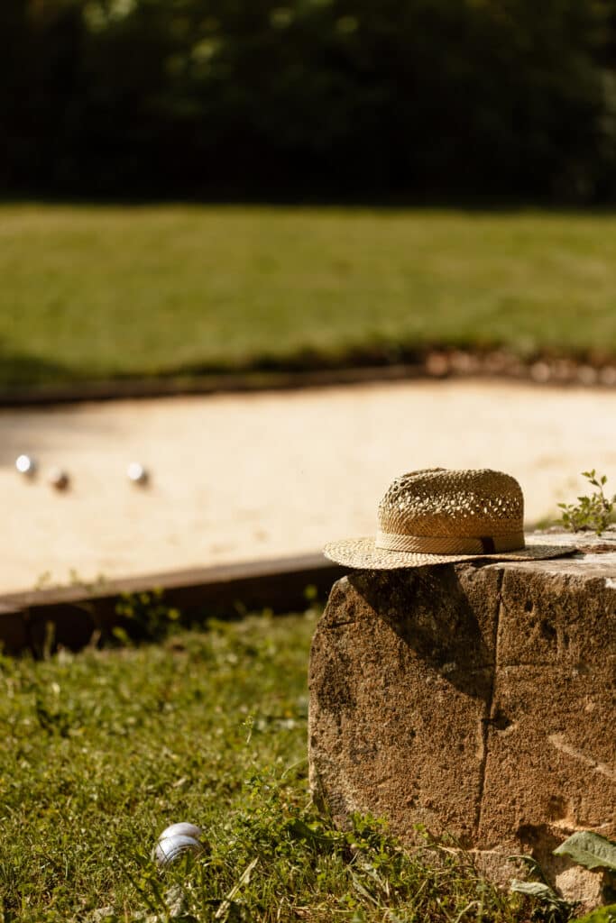Pétanque d'été: Chapeau de paille sur pierre au soleil Chapeau de paille sur un bloc de pierre près d'un terrain de pétanque ensoleillé avec des boules éparses. Ambiance estivale décontractée.