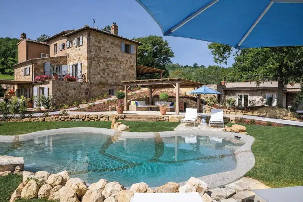 Villa de rêve en pierre: Piscine turquoise et jardin toscan. Luxueuse villa toscane en pierre jaune, dotée d'une piscine aux formes libres, d'un jardin verdoyant et d'une zone de détente sous une pergola ensoleillée.