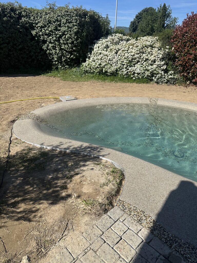 Aménagement piscine lagon : design naturel et moderne Piscine lagon aux formes organiques, eau turquoise et bordure minérale dans un jardin en aménagement.