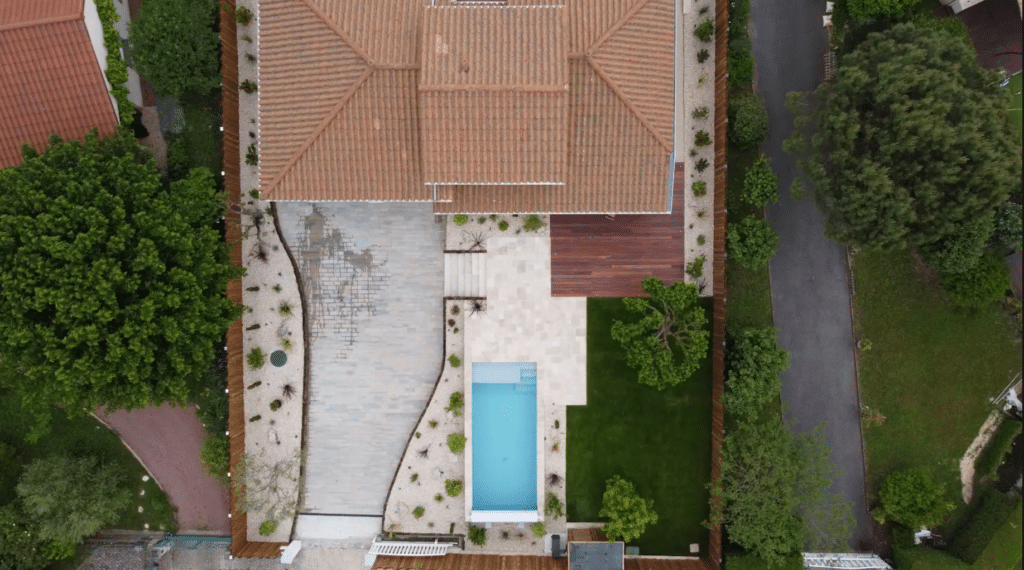 Vue aérienne d'une villa avec piscine rectangulaire, terrasse bois et jardin paysager moderne.